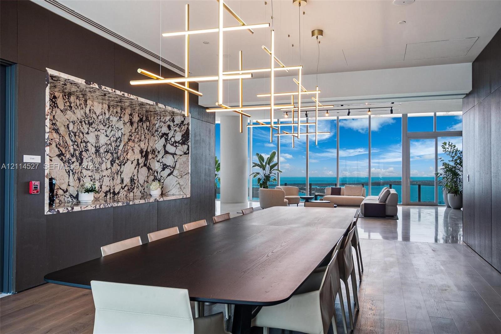 Floor-to-ceiling glass windows, custom built-in cabinetry featuring patterned stone inlay, linear geometric pendant lighting, wood-finish flooring, and polished flooring surfaces