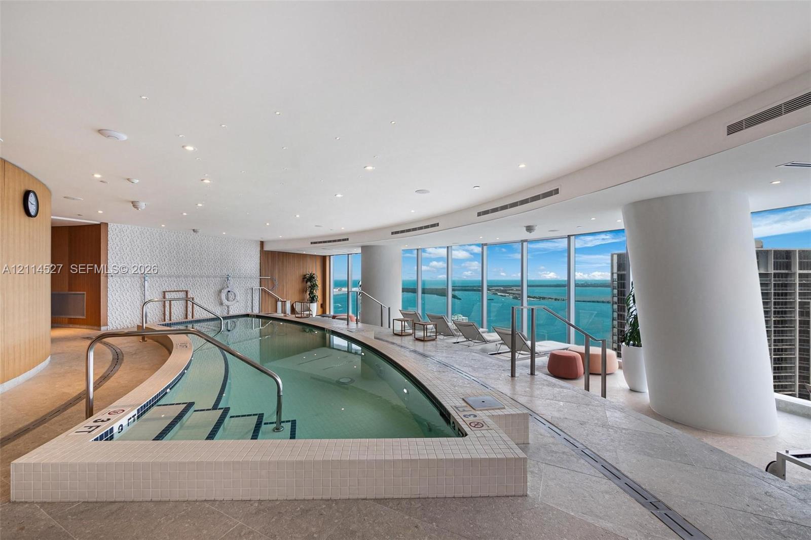 Indoor pool area featuring floor-to-ceiling windows, stone tile flooring, recessed ceiling lighting, and custom curved architectural columns