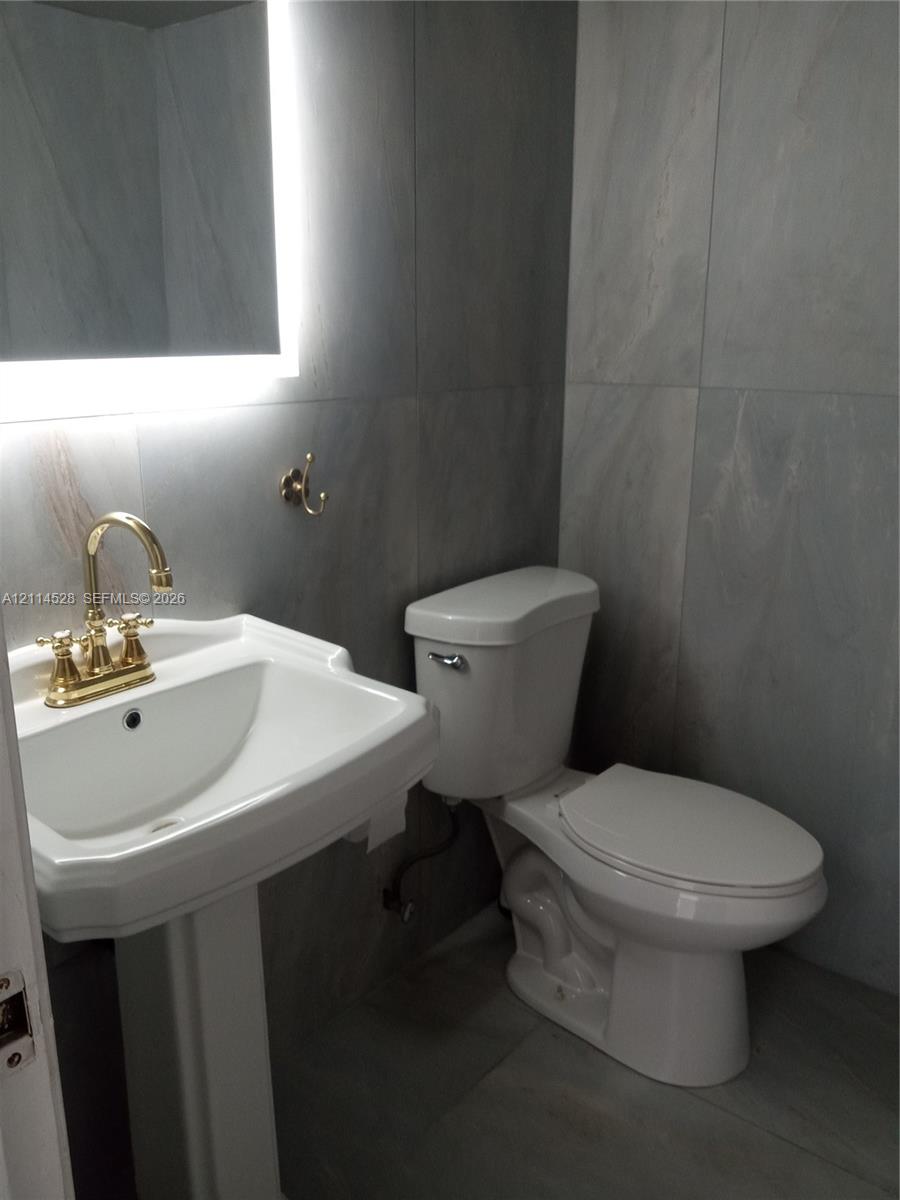 Pedestal sink with brass finish faucet, large-format grey wall tiling, and backlit vanity mirror