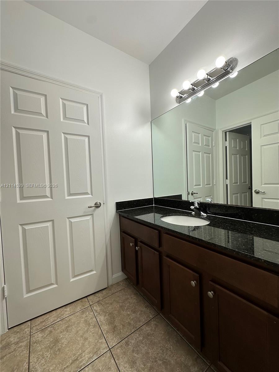Dark wood-finish cabinetry topped with a stone vanity surface, an integrated undermount sink, a full-width mirror, and multi-bulb vanity lighting