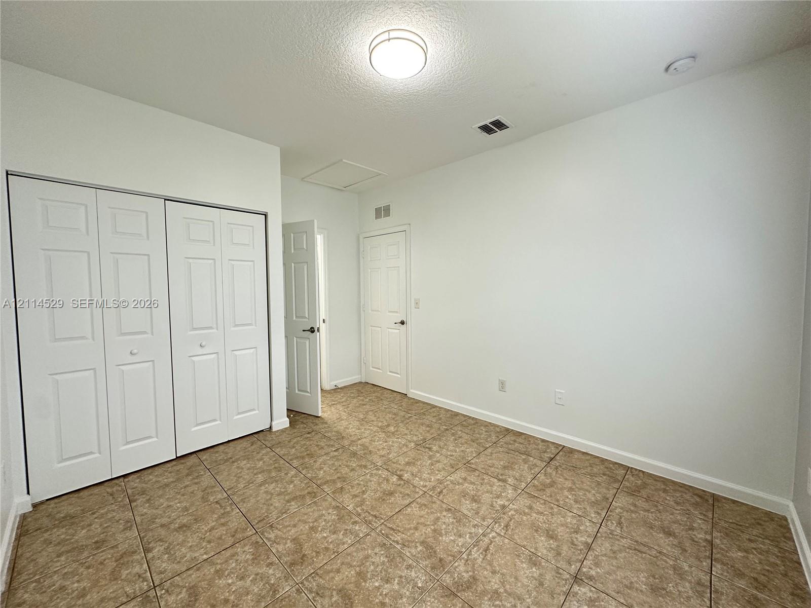 Neutral-toned tile flooring, recessed ceiling lighting, and a multi-panel closet door