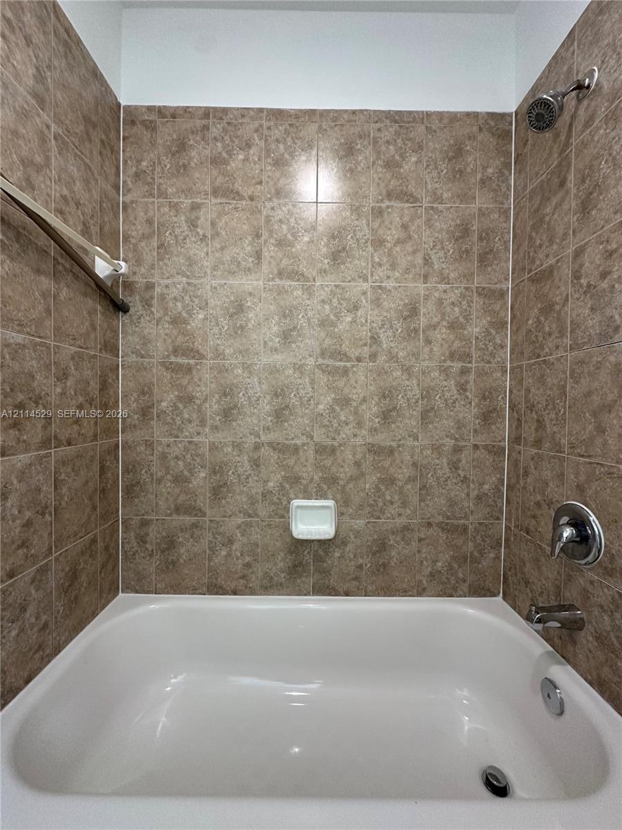 Bathtub surround featuring floor-to-ceiling square ceramic tiles, a built-in recessed soap dish, and polished chrome shower and tub fixtures
