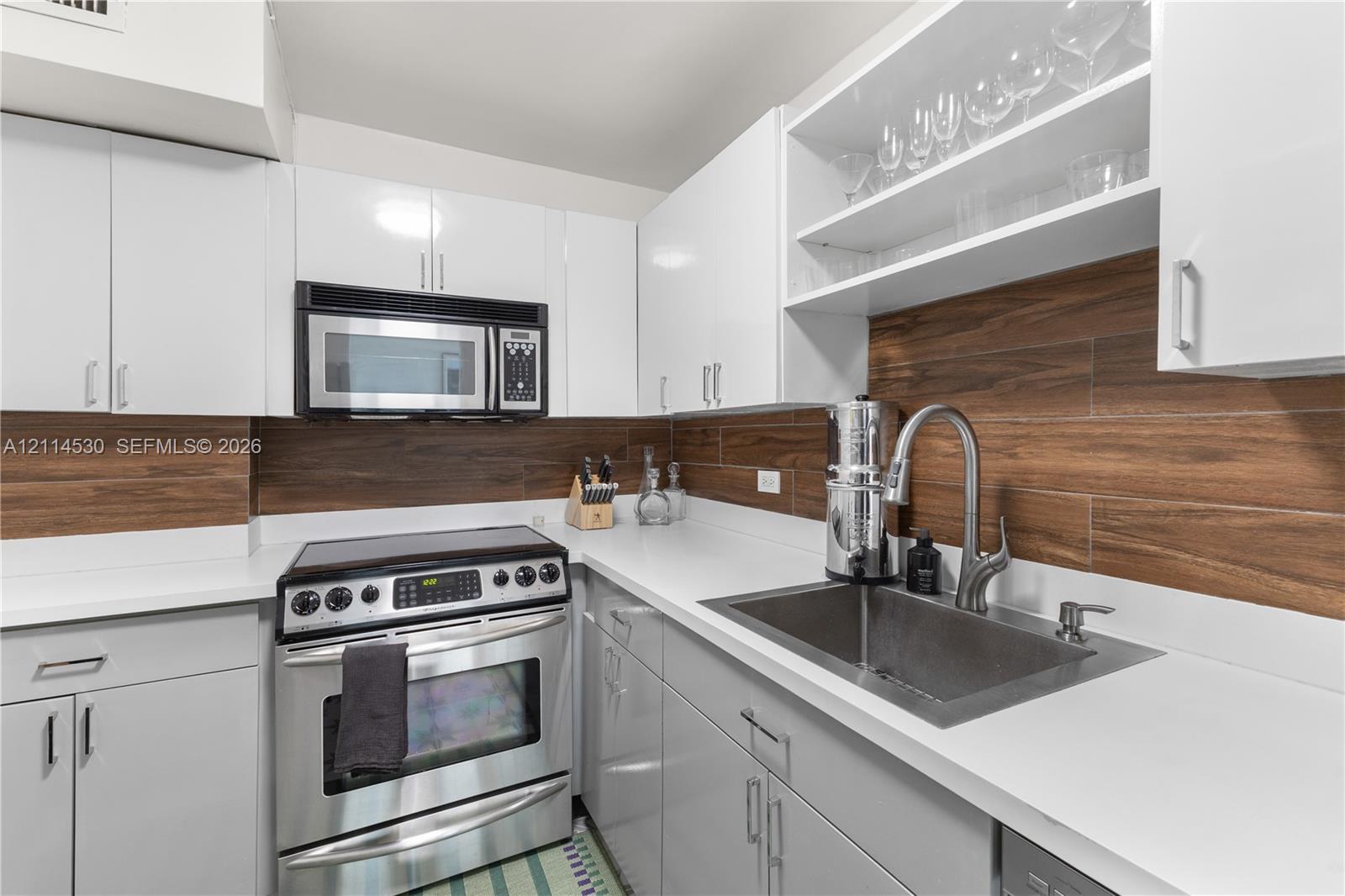 Kitchen featuring white flat-panel cabinetry, quartz countertops, stainless steel appliances, wood-finish tile backsplash, and open shelving