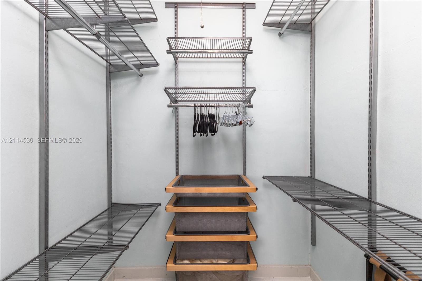 Walk-in closet featuring adjustable metal wire shelving, wall-mounted vertical standards, and a central built-in unit with four slide-out fabric storage baskets framed in wood trim