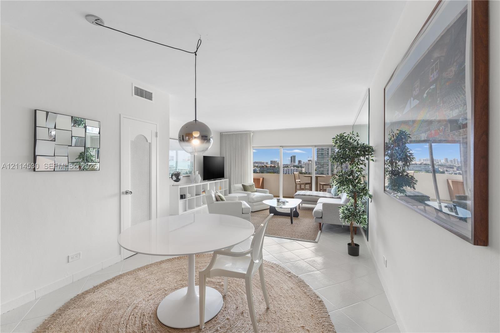 Living area featuring large-format ceramic tile flooring, floor-to-ceiling glass sliding doors, a polished metallic spherical pendant light, and a full-wall mirror