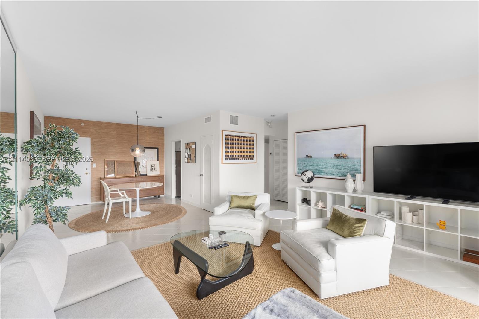 Open-concept living space featuring high ceilings, light-toned flooring, wall-to-wall mirror paneling, and a distinct wood-paneled accent wall