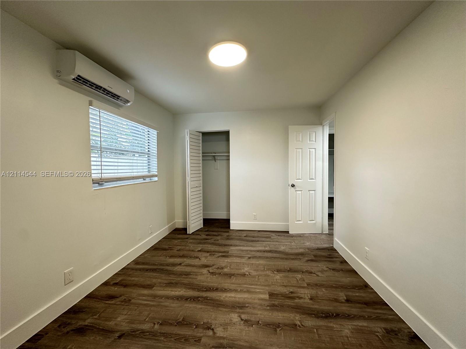 Interior space featuring wood-finish flooring, a wall-mounted ductless mini-split climate control system, a closet with louvered doors, a flush-mount ceiling light, and a six-panel door