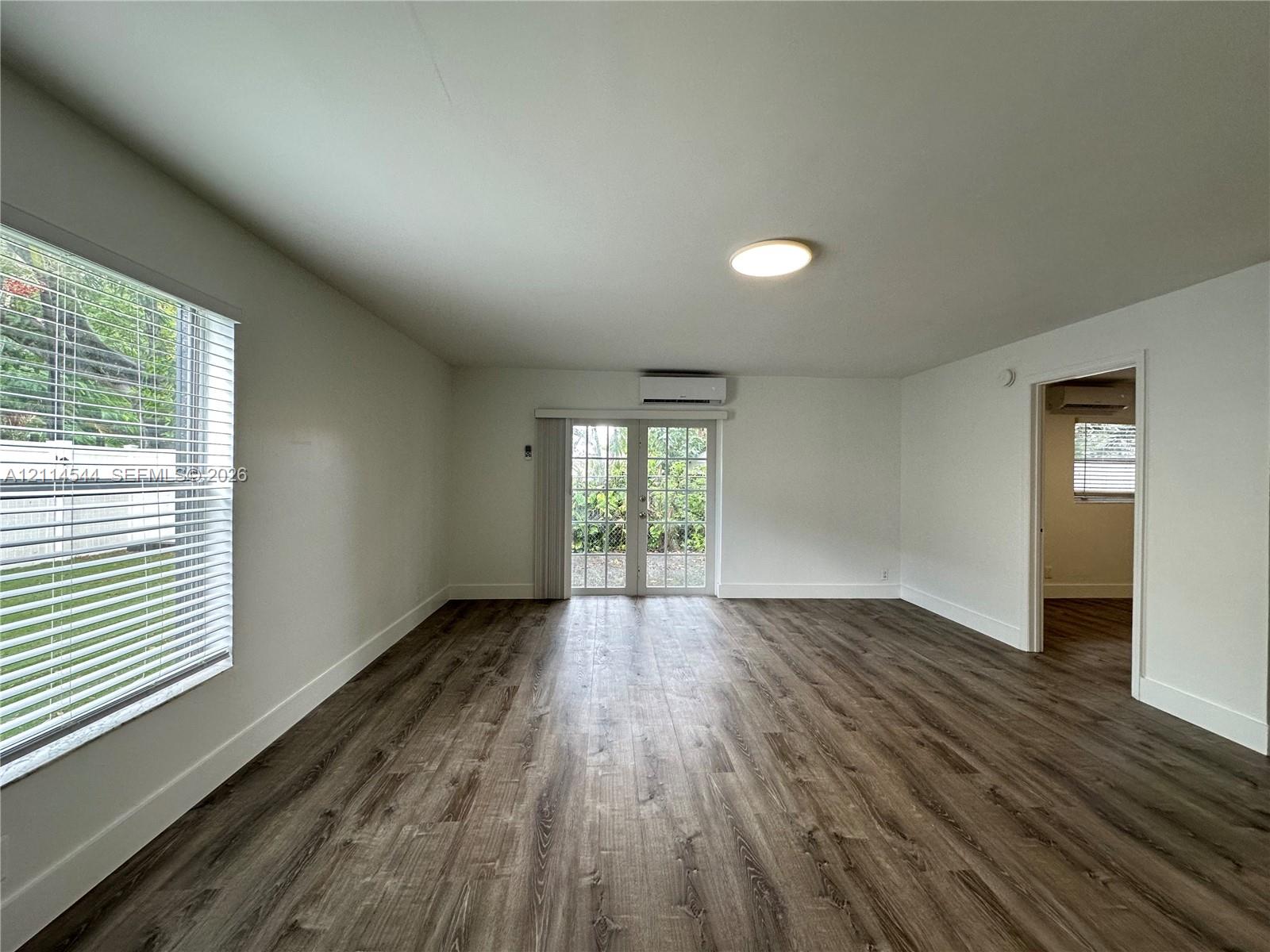 Wood-finish flooring, glass-paneled double doors, wall-mounted ductless air conditioning unit, and horizontal blind window treatments Wood-finish flooring, glass-paneled double doors, wall-mounted ductless air conditioning unit, and horizontal blind window treatments