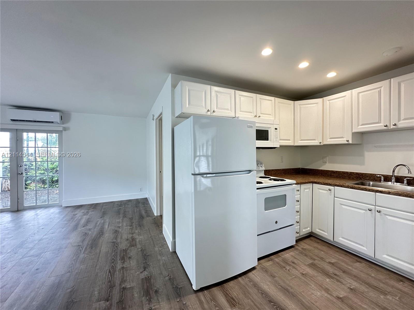 Kitchen featuring white shaker-style cabinetry, speckled countertops, stainless steel sink, wood-finish flooring, and glass-paneled patio door Kitchen featuring white shaker-style cabinetry, speckled countertops, stainless steel sink, wood-finish flooring, and glass-paneled patio door