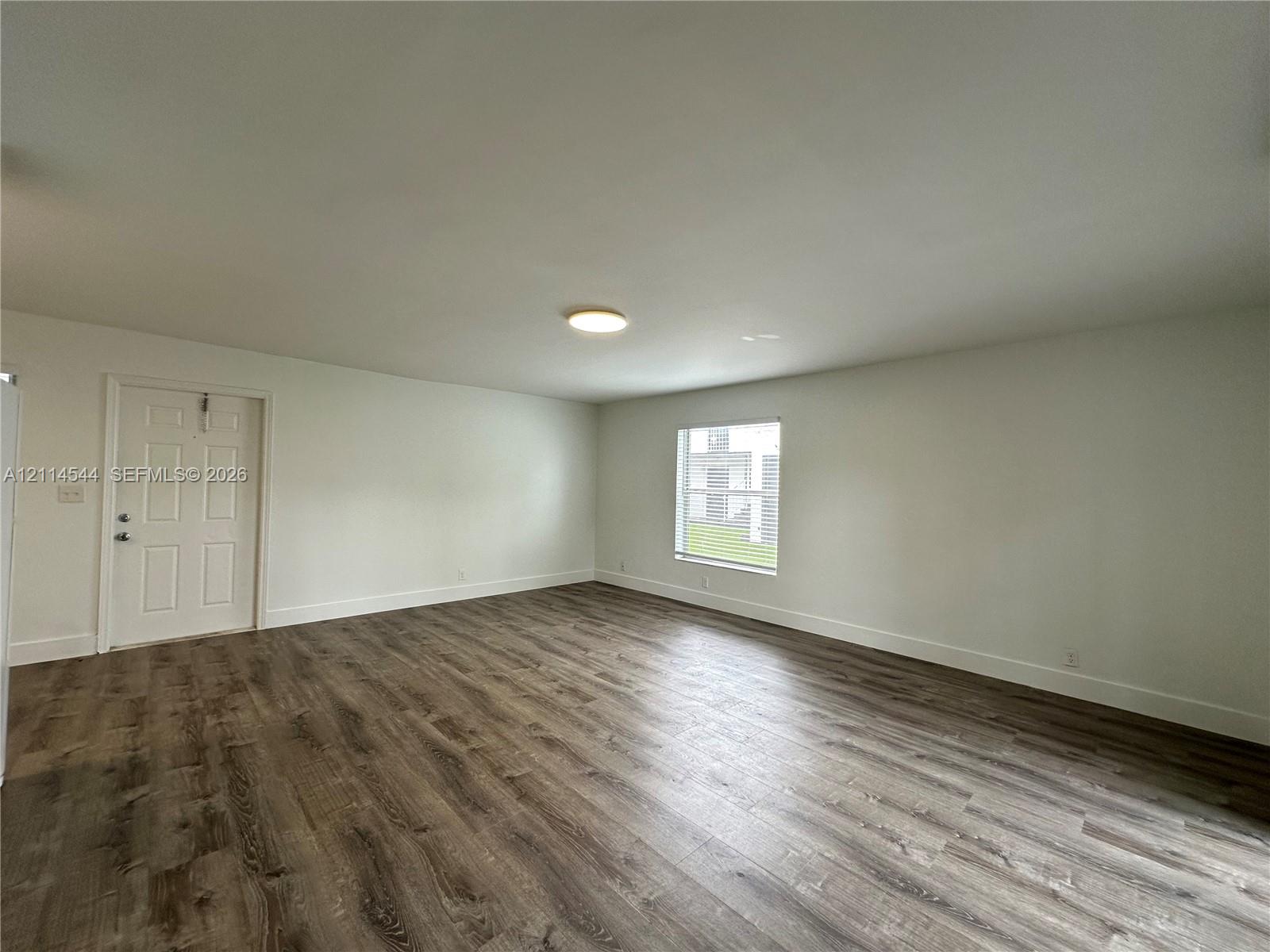 Interior space featuring wood-finish flooring, white walls, a flush-mount ceiling light, and a single-panel window Interior space featuring wood-finish flooring, white walls, a flush-mount ceiling light, and a single-panel window