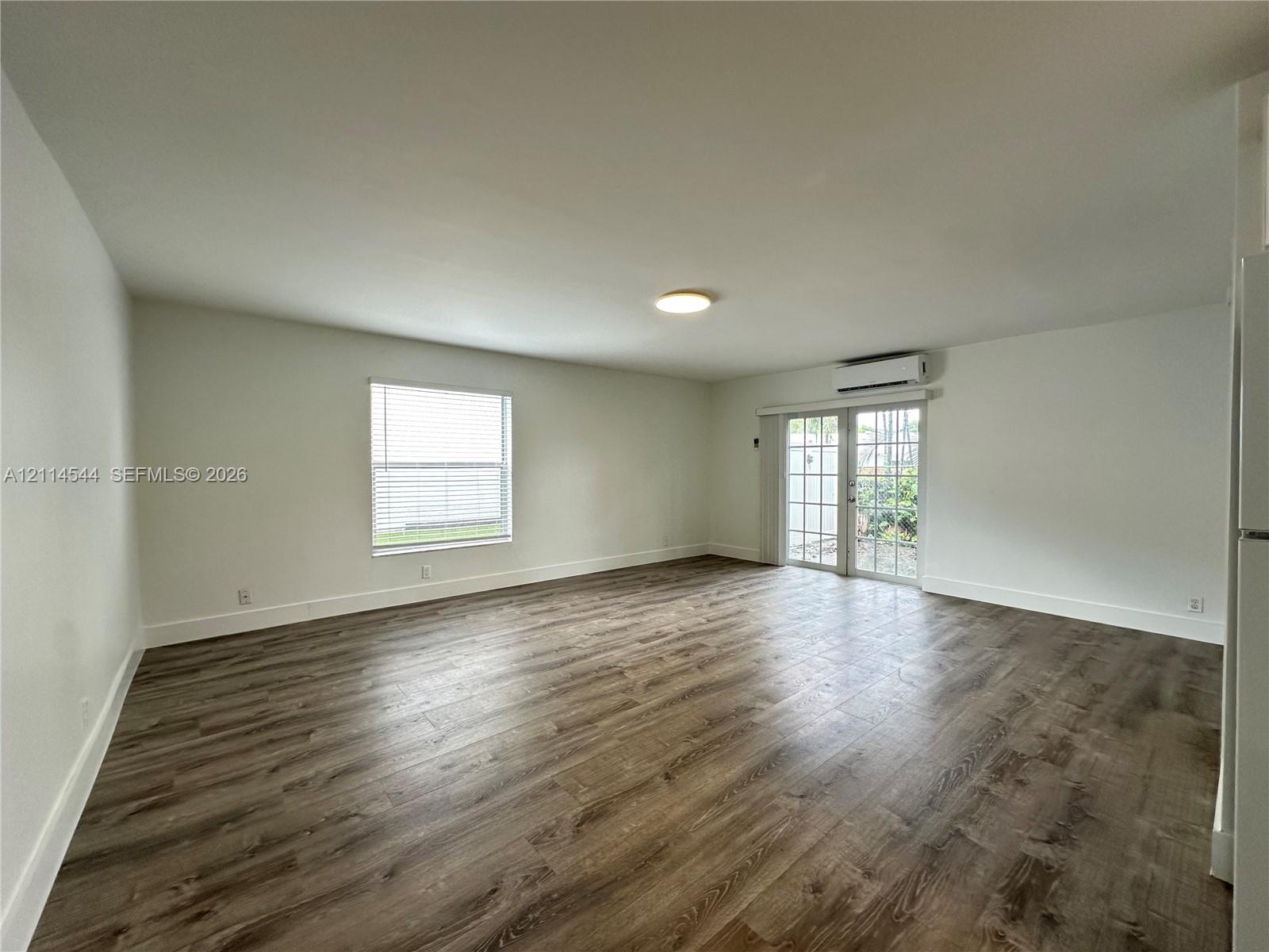 Open-concept interior featuring wood-finish flooring, a single-hung window with blinds, and glass-paned French doors Open-concept interior featuring wood-finish flooring, a single-hung window with blinds, and glass-paned French doors