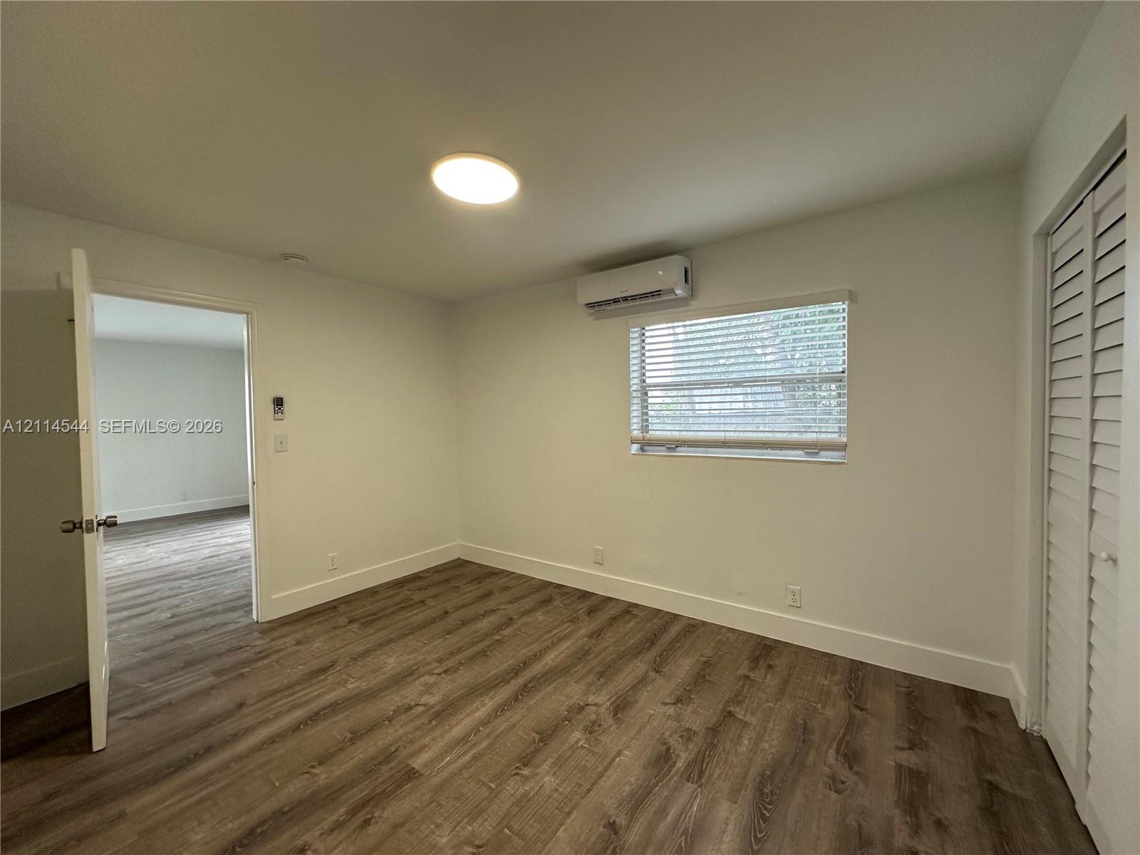 Room featuring wood-finish flooring, a wall-mounted ductless air conditioning unit, recessed ceiling lighting, and a closet with louvered bi-fold doors