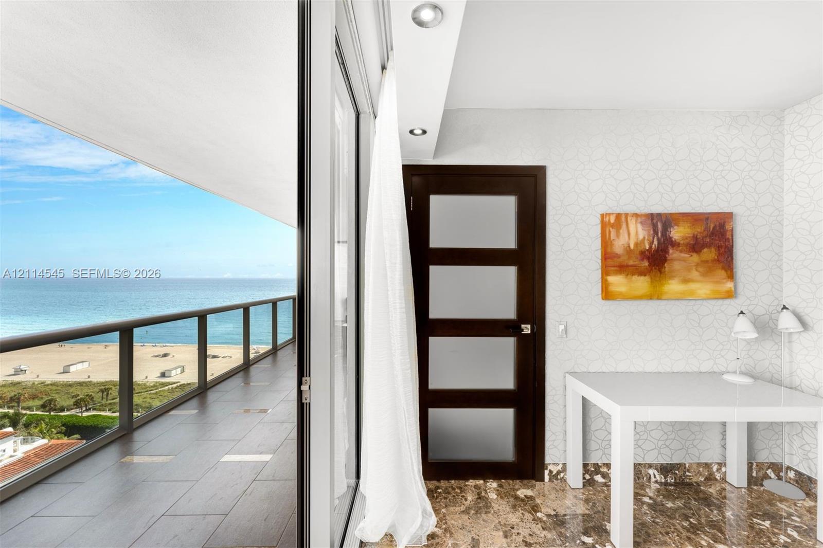 Expansive balcony with floor-to-ceiling glass sliding doors, dark tile flooring, glass panel railing, and ocean backdrop