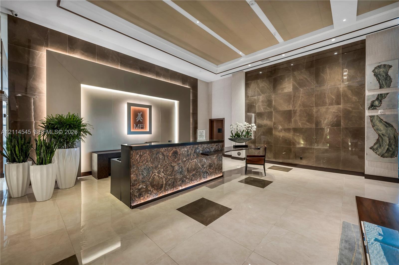 Grand lobby featuring large-format tile flooring, oversized stone-clad feature walls, a backlit stone reception desk, and a tiered tray ceiling with recessed architectural lighting