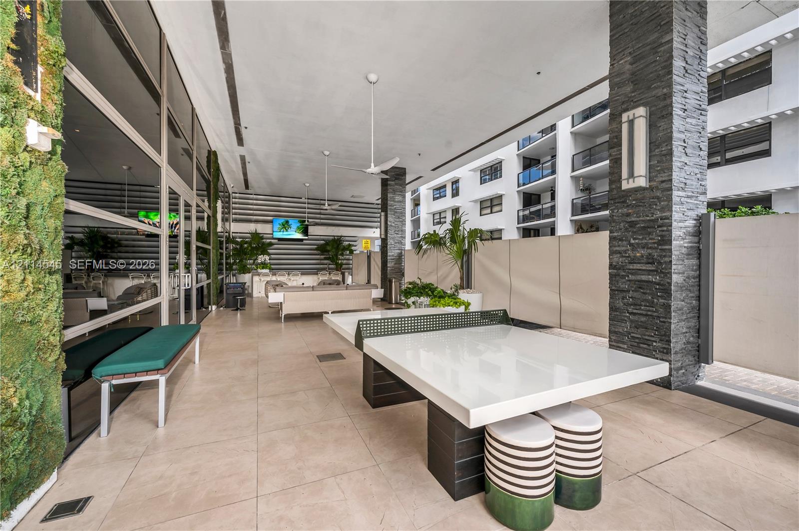 Covered outdoor terrace featuring large-format tile flooring, stacked stone column cladding, and preserved moss wall paneling, complemented by dual ceiling fans and wall-mounted lighting