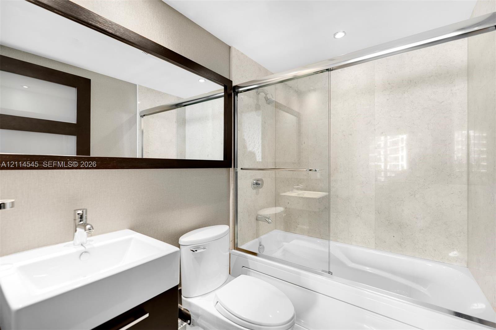 Bathroom featuring a vanity with an integrated rectangular sink, large framed mirror, soaking tub with glass sliding enclosure, and light-toned tile surround