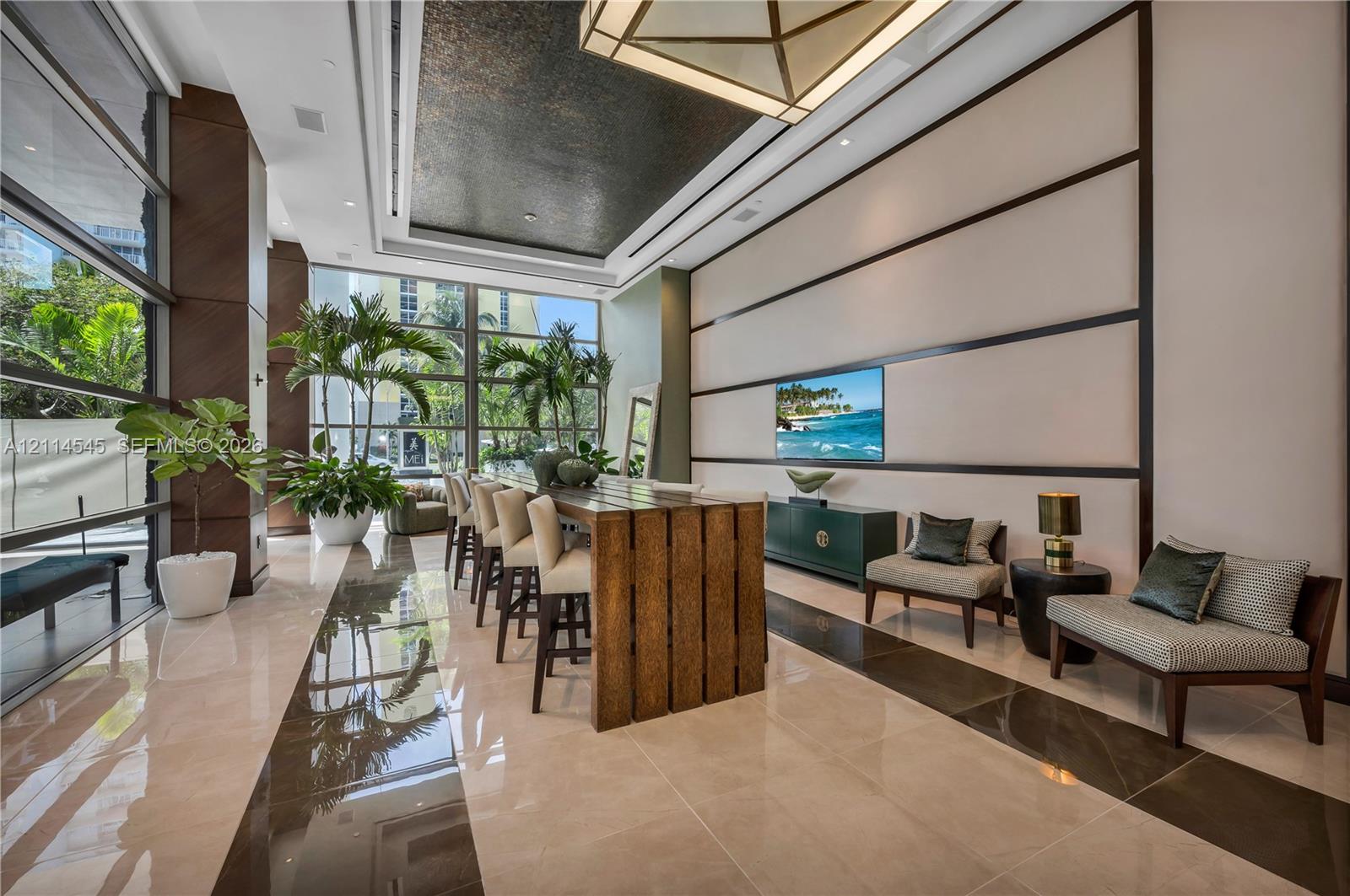 Grand lobby featuring floor-to-ceiling windows, polished stone flooring, a textured recessed ceiling with geometric lighting, and decorative wall paneling
