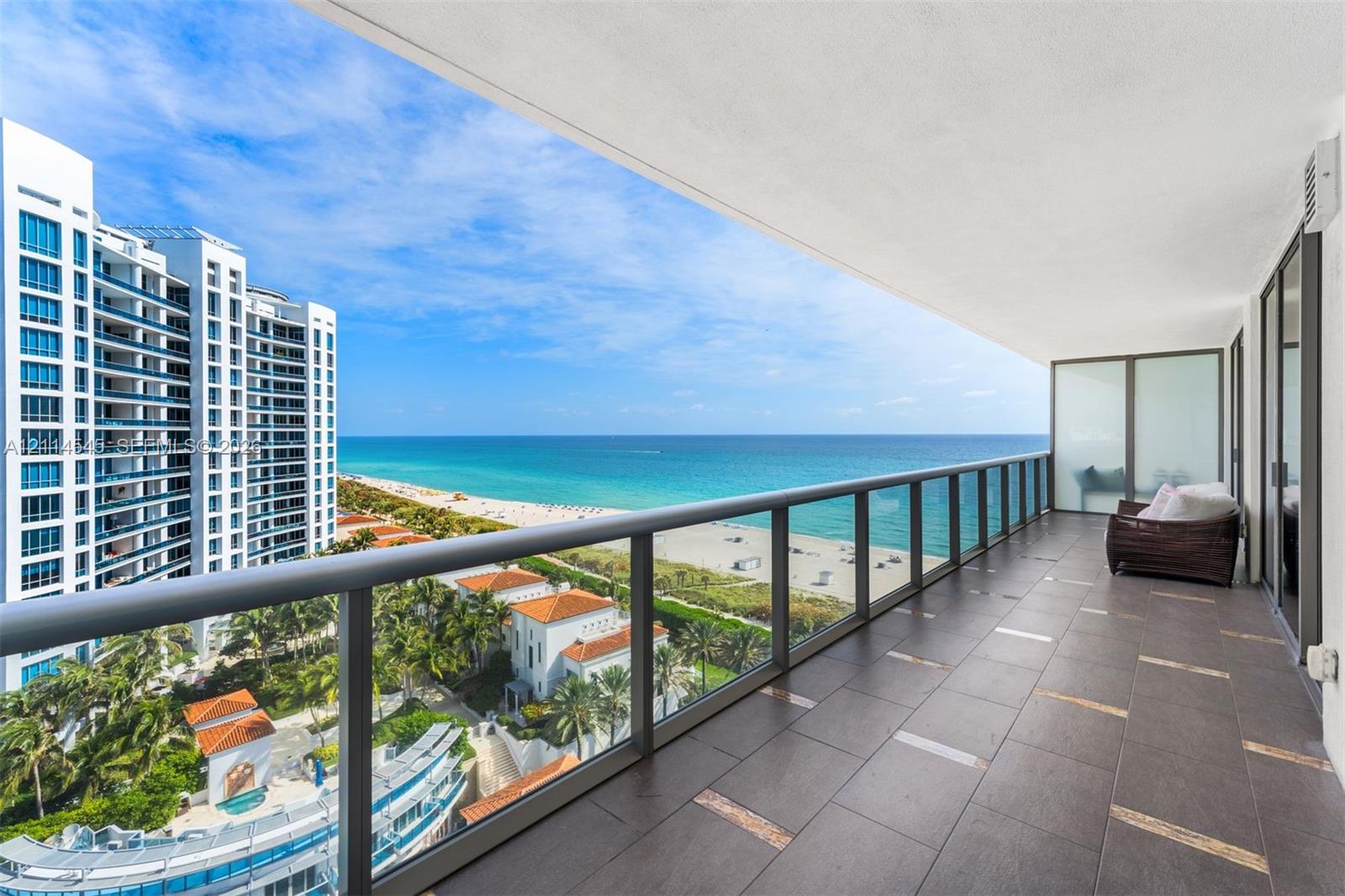 Spacious covered terrace featuring large-format porcelain tile flooring and metal-framed glass railings with ocean and coastal frontage