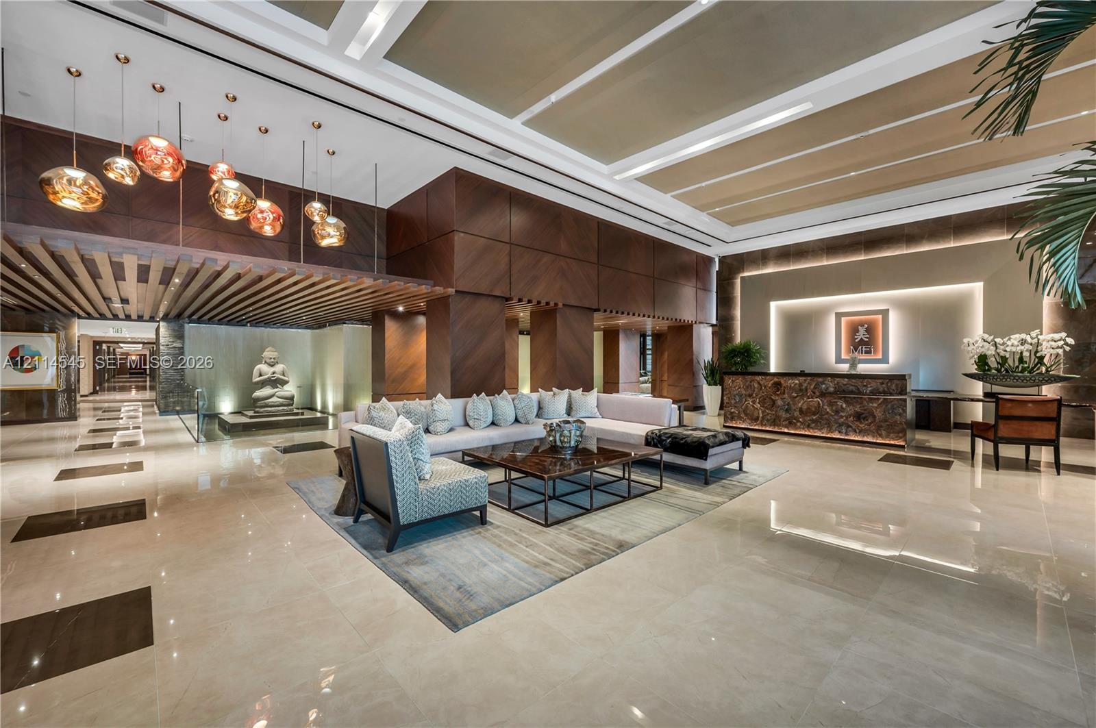 Grand lobby featuring high coffered ceilings, large-format tile flooring, wood-paneled walls, an integrated reception desk with stone detailing, and multi-pendant lighting fixtures