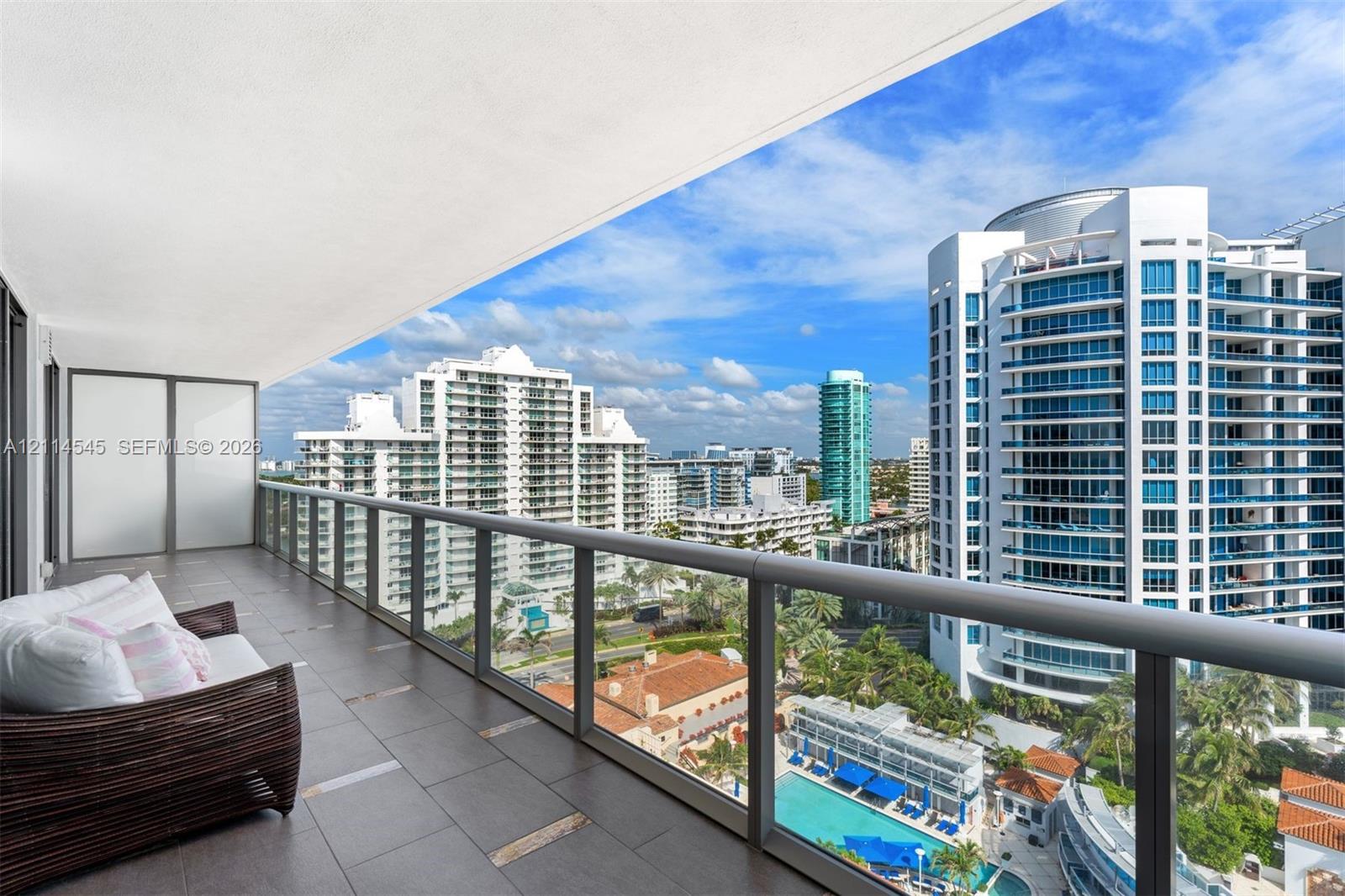 Covered terrace featuring dark tile flooring and a glass railing system, overlooking urban architecture and a swimming pool