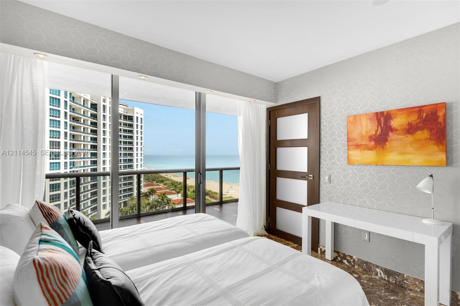 Floor-to-ceiling glass sliding doors, private balcony with metal railing, oceanic scenery, patterned wall covering, and stone-finish flooring