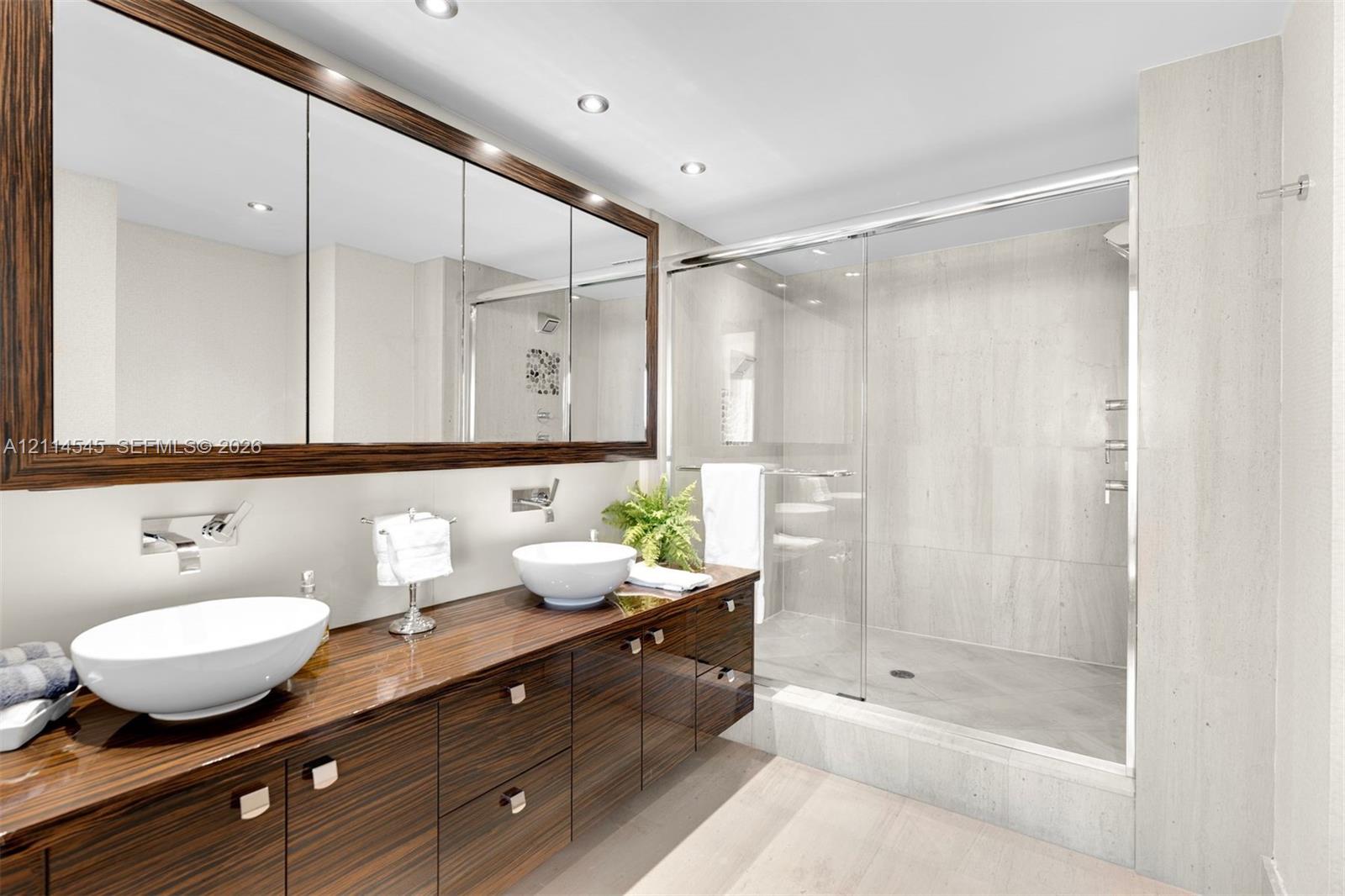 Dual-sink vanity featuring a dark wood finish, two white vessel sinks, wall-mounted chrome faucets, and an expansive tri-panel medicine cabinet
