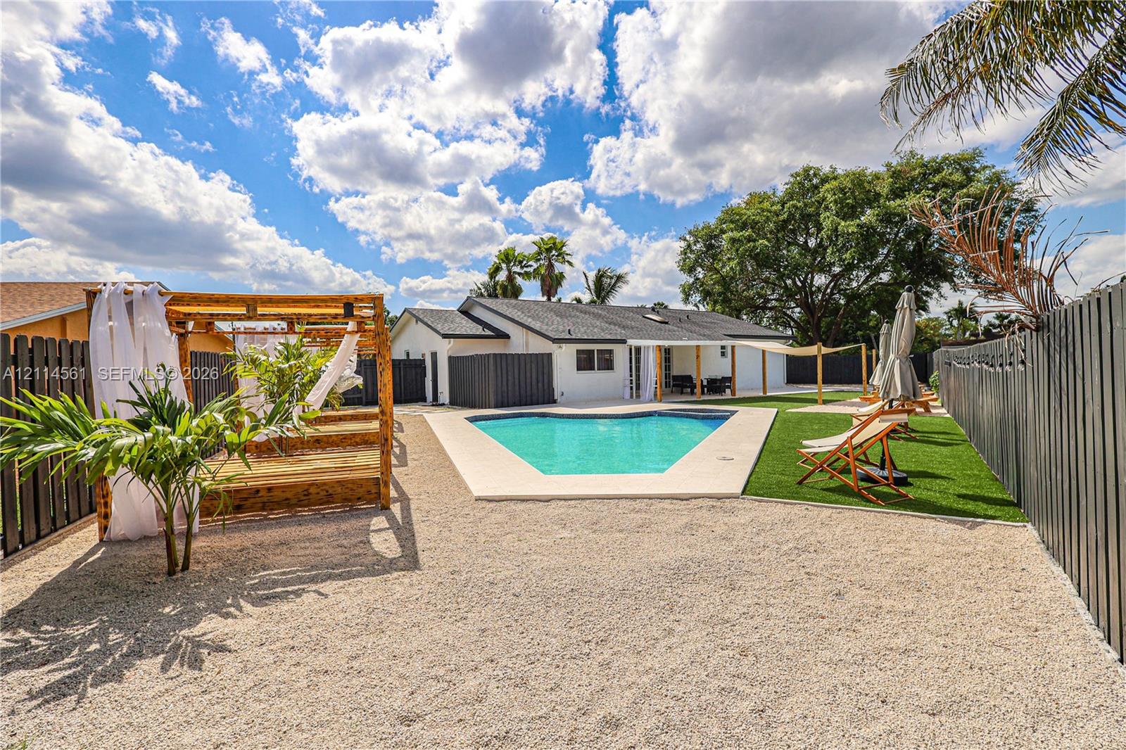 Private backyard featuring an in-ground swimming pool, custom wood pergola, gravel ground cover, artificial turf lawn, and perimeter privacy fencing