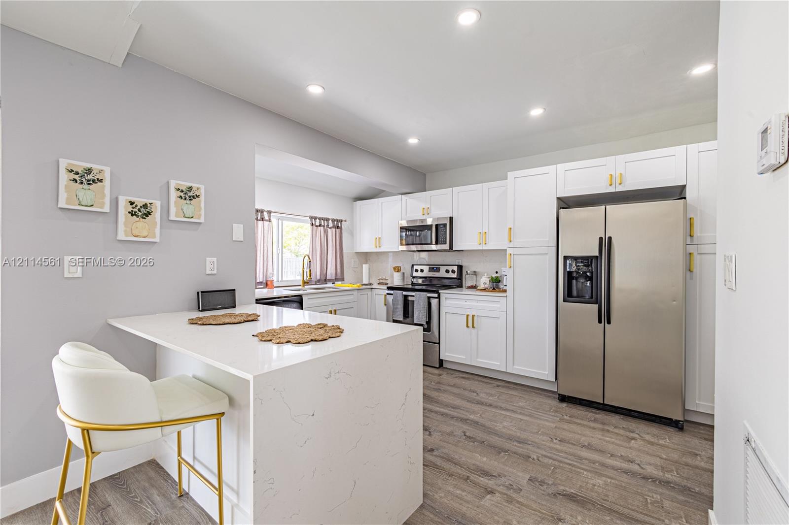 Kitchen featuring white shaker-style cabinetry, quartz countertops with waterfall edge, stainless steel appliances, recessed lighting, and wood-finish flooring