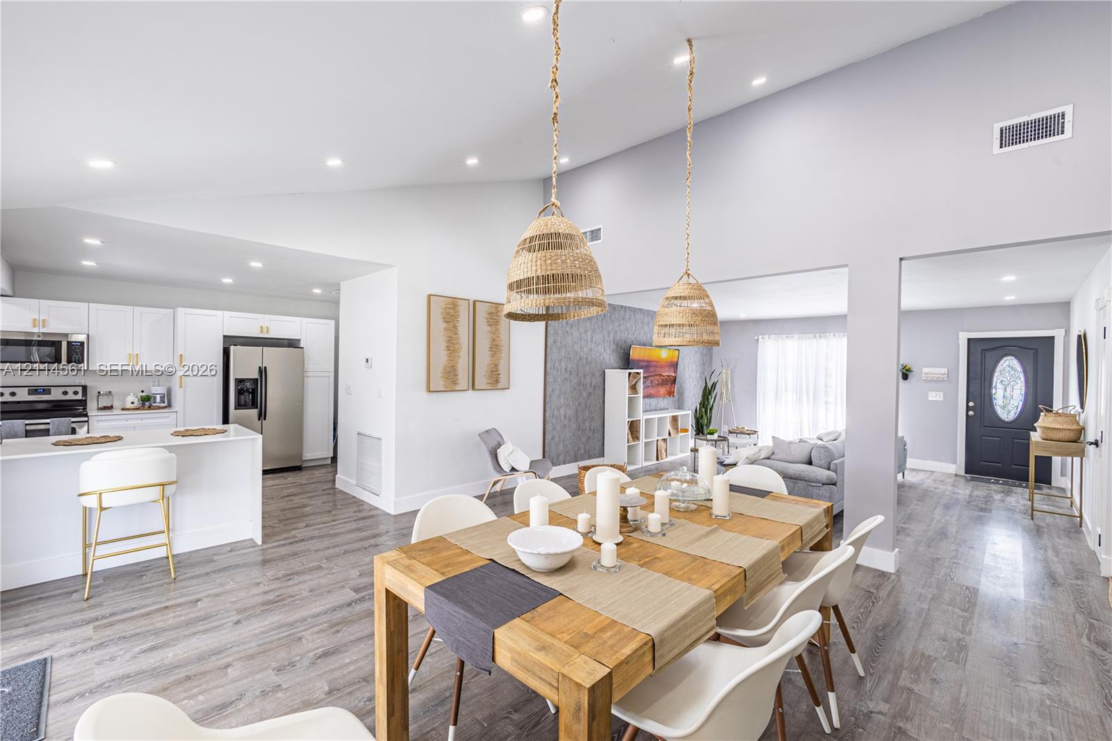 Vaulted ceilings, open-concept kitchen with white cabinetry and stainless steel appliances, wood-finish flooring, and natural-textured pendant lighting