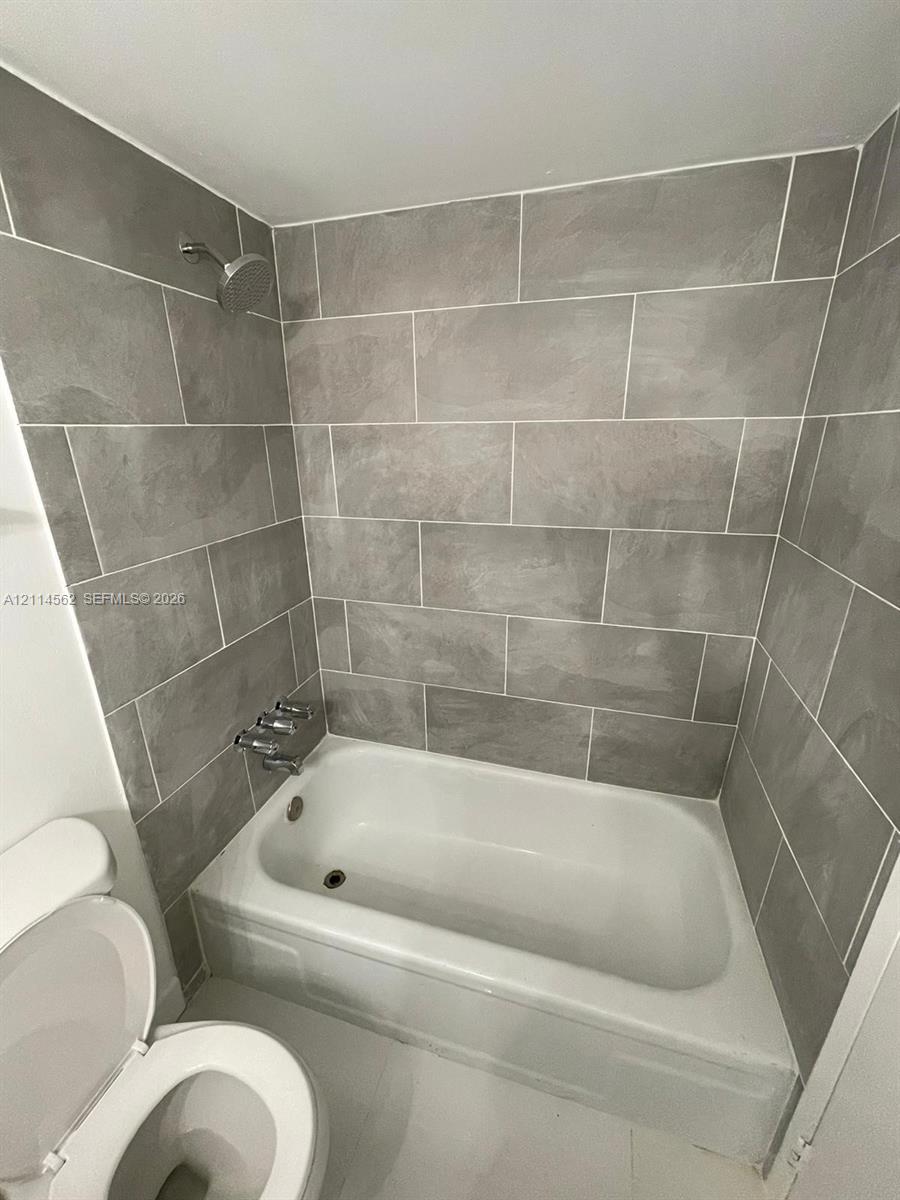 Full-height grey tile tub surround, white porcelain bathtub, chrome wall-mounted shower head, and chrome faucet hardware