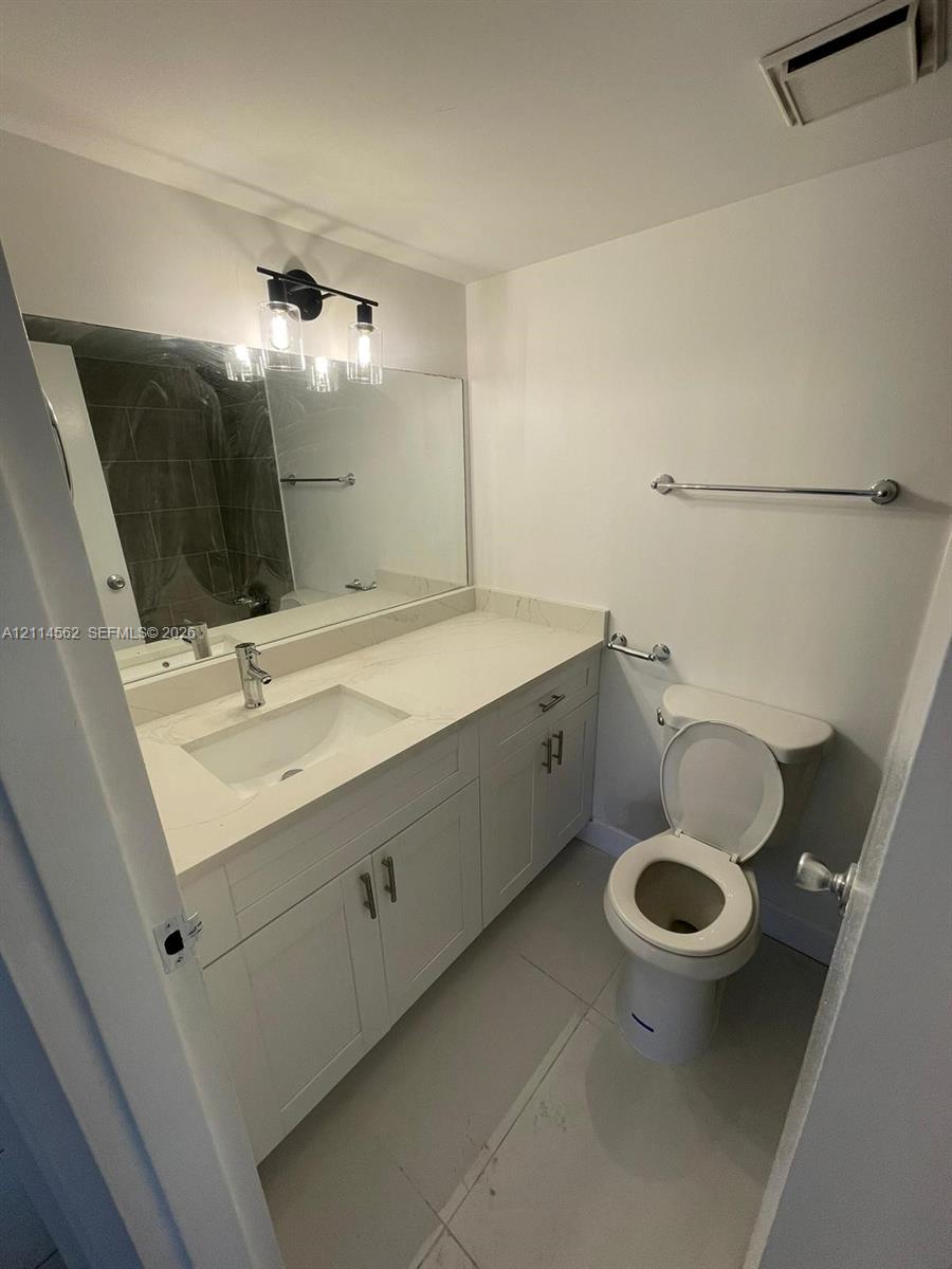 Bathroom featuring a vanity with integrated sink, stone-finish countertop, white cabinetry with metallic hardware, wall-mounted three-light fixture, and large vanity mirror