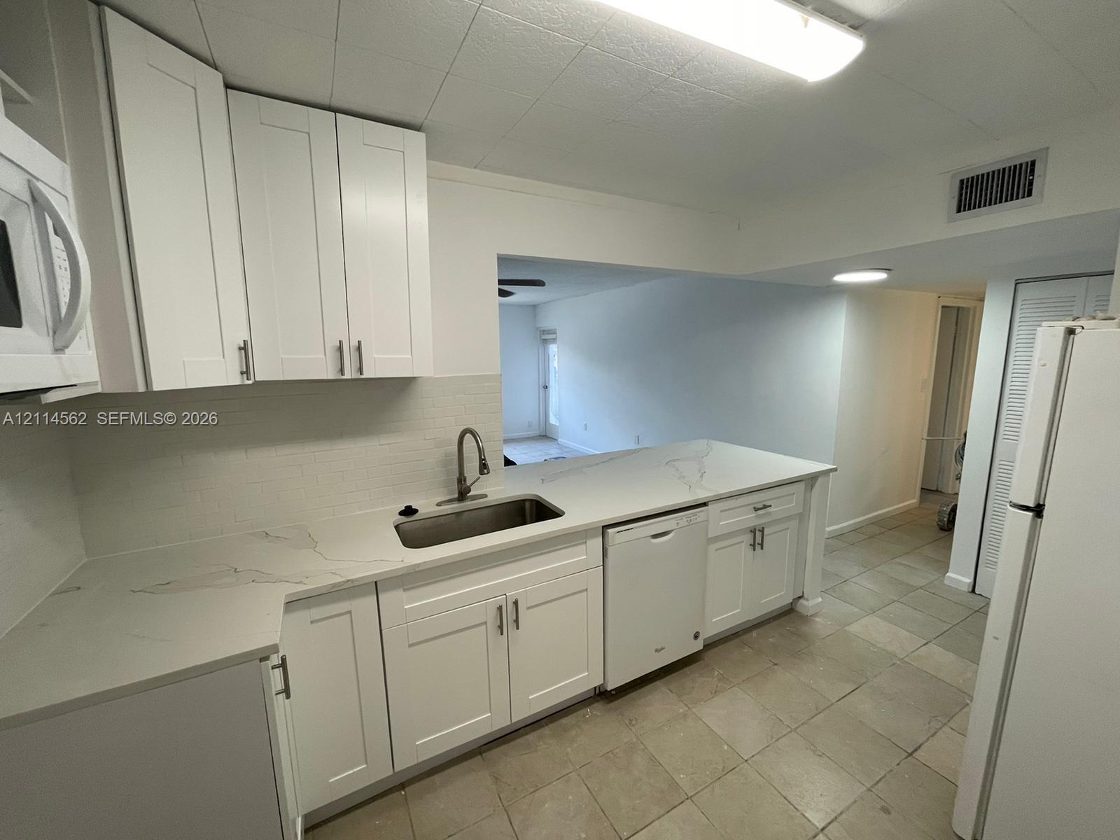 Kitchen featuring white cabinetry, quartz countertops with veining, an undermount stainless steel sink with a high-arch faucet, and a dishwasher
