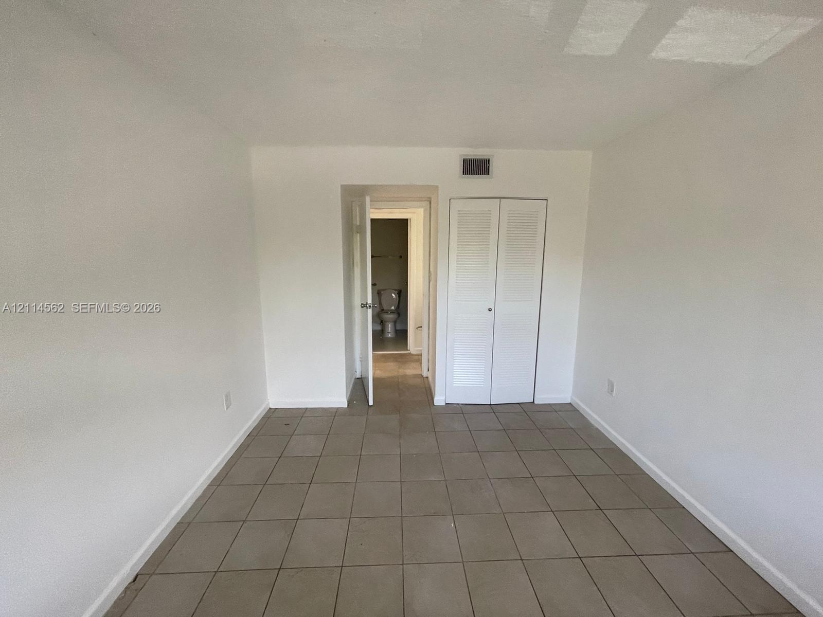 Neutral-toned tile flooring, white interior walls, and built-in closet with double louvered doors
