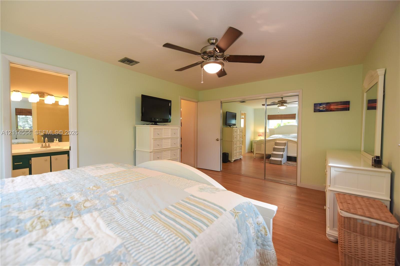 Room featuring wood-finish flooring, a ceiling fan with integrated lighting, and mirrored closet doors