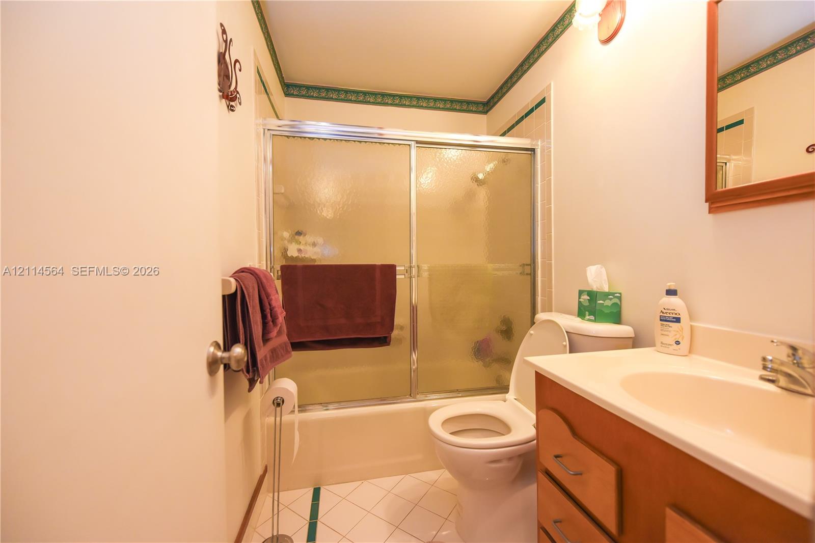 Bathroom featuring a vanity with an integrated sink and chrome faucet, a tub-shower combination with a sliding glass enclosure, and tile flooring