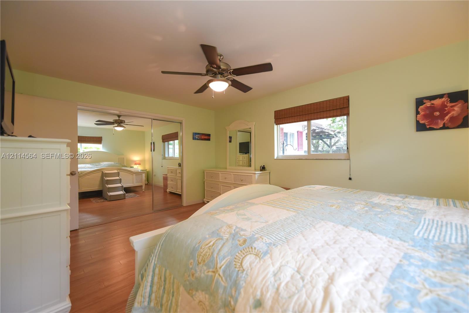 Wood-finish flooring, ceiling fan with integrated lighting, mirrored sliding closet doors, and woven wood window treatments