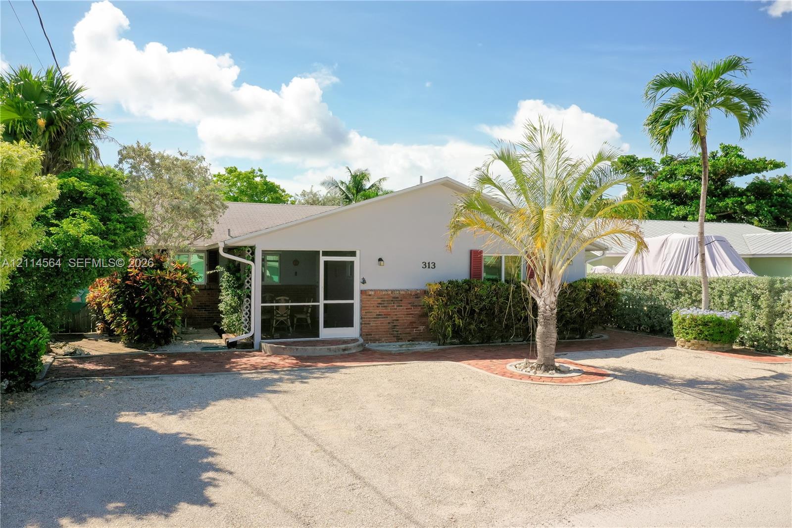 Single-story exterior featuring a screened-in porch, brick facade detailing, and a crushed stone driveway Single-story exterior featuring a screened-in porch, brick facade detailing, and a crushed stone driveway