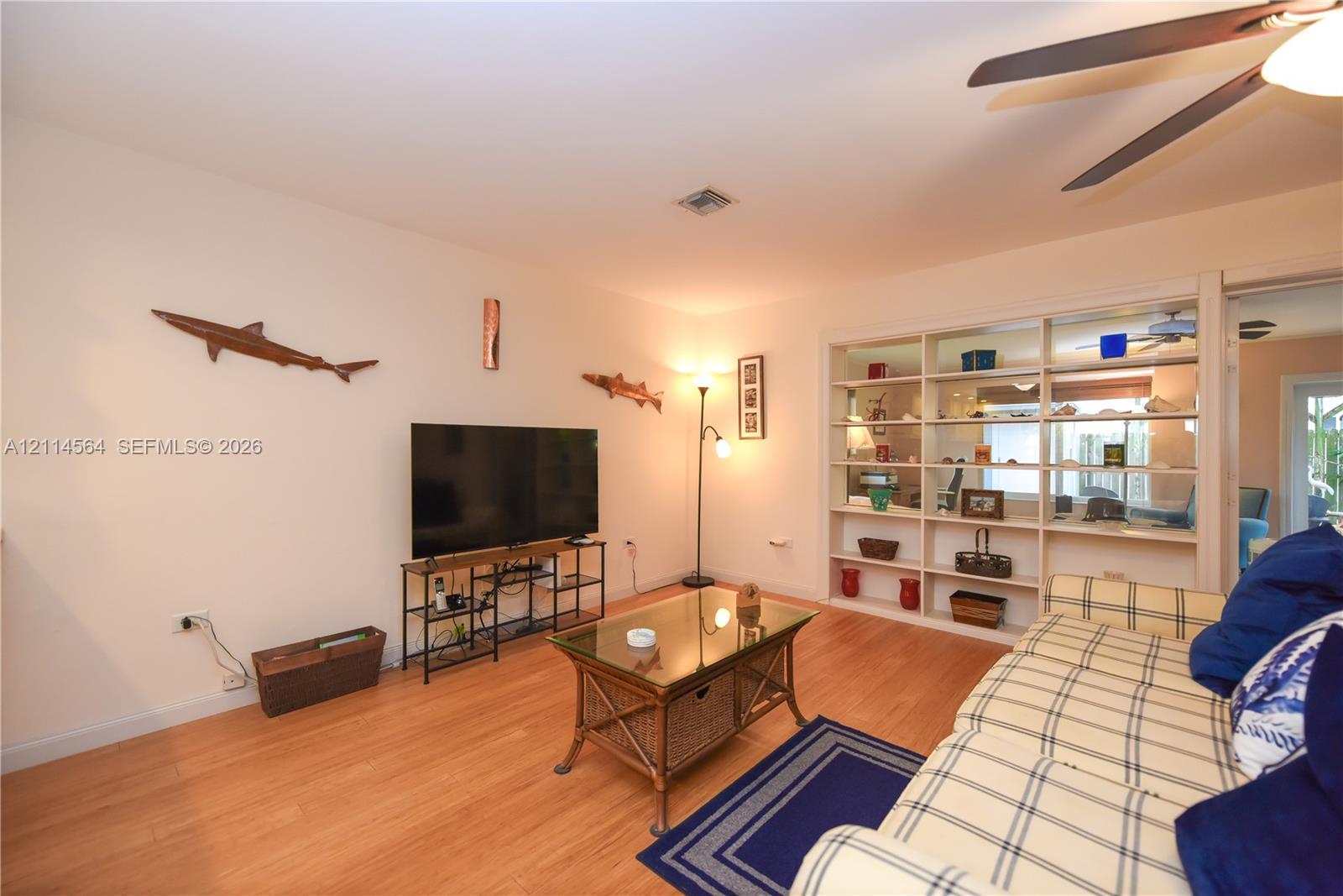 Living area featuring wood-finish flooring, recessed ceiling lighting, a dedicated ceiling fan, and built-in floor-to-ceiling shelving