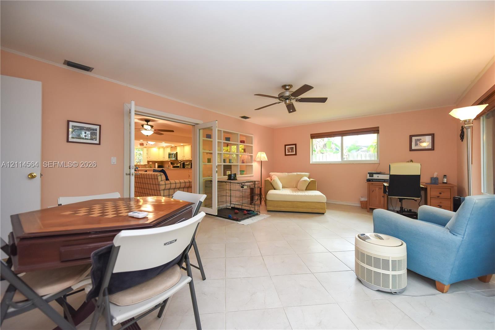 Open-concept interior featuring light-toned tile flooring, double French doors, a built-in recessed shelving unit, and a ceiling fan
