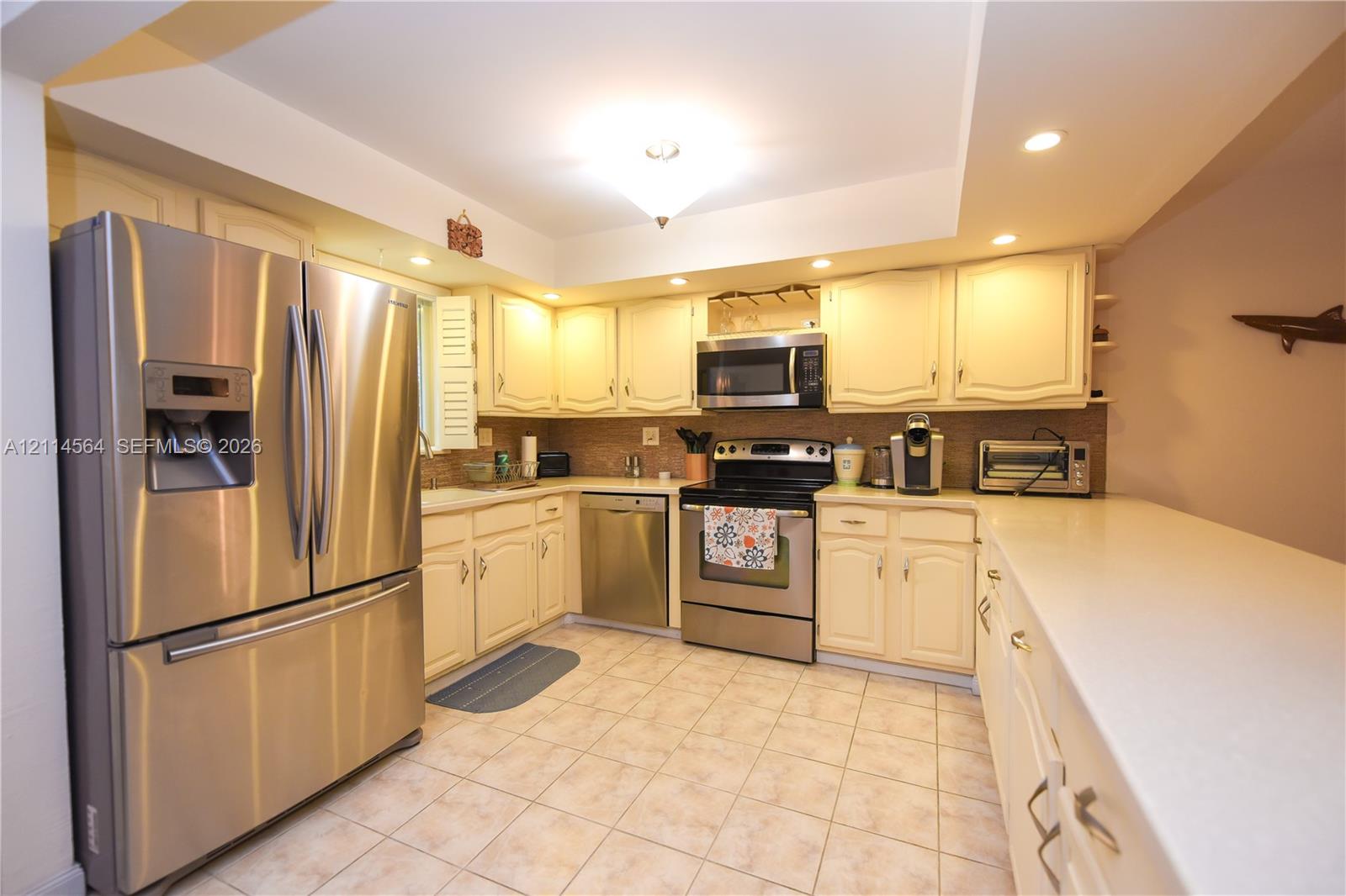 Kitchen featuring stainless steel appliances, light-toned cabinetry, solid surface countertops, recessed lighting, and tile flooring