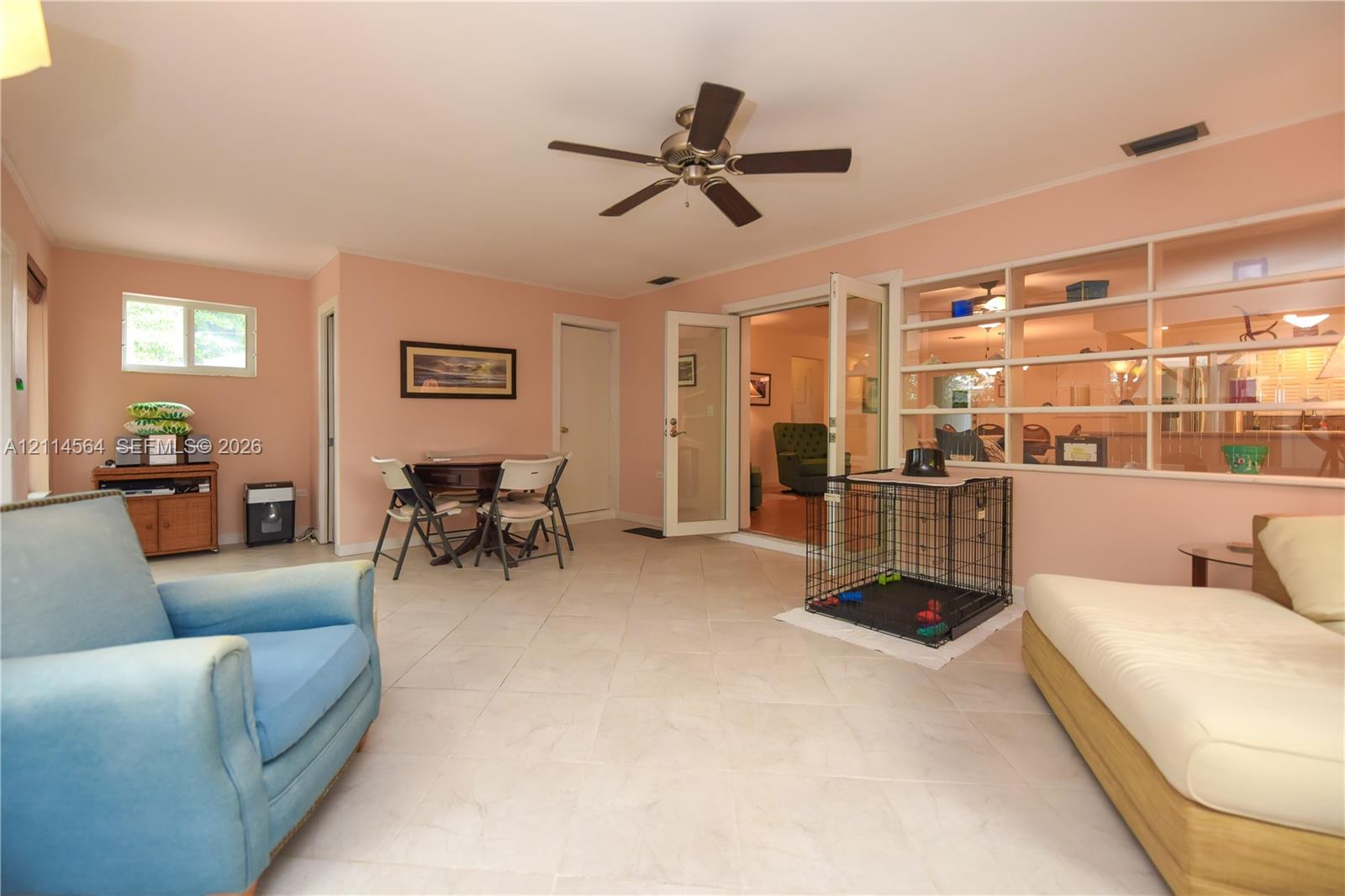 Open-concept interior featuring large-format tile flooring, a ceiling fan, double French doors, and a built-in multi-level display shelving unit