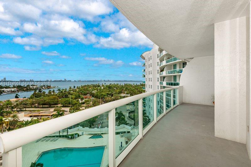 Covered balcony featuring a glass panel railing, concrete flooring, and water scenery