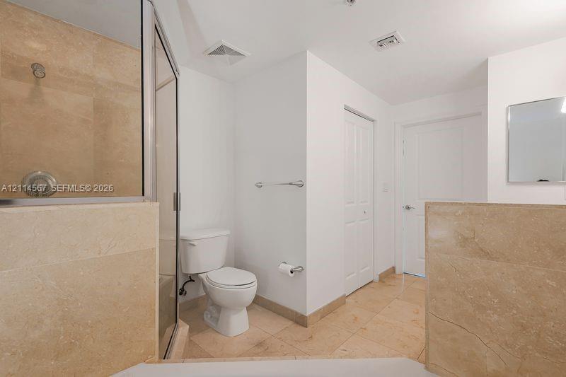 Bathroom featuring natural stone tile flooring and shower surround, glass-enclosed shower, wall-mounted mirror, and metal fixtures