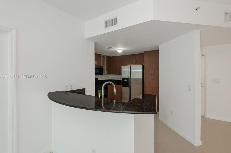 Kitchen featuring a curved breakfast bar, dark stone countertops, wood-finish cabinetry, and stainless steel appliances