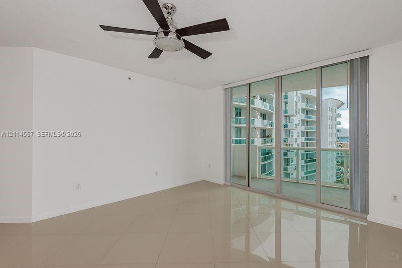 Neutral-toned tile flooring, floor-to-ceiling glass sliding doors, and a ceiling-mounted fan with integrated light fixture