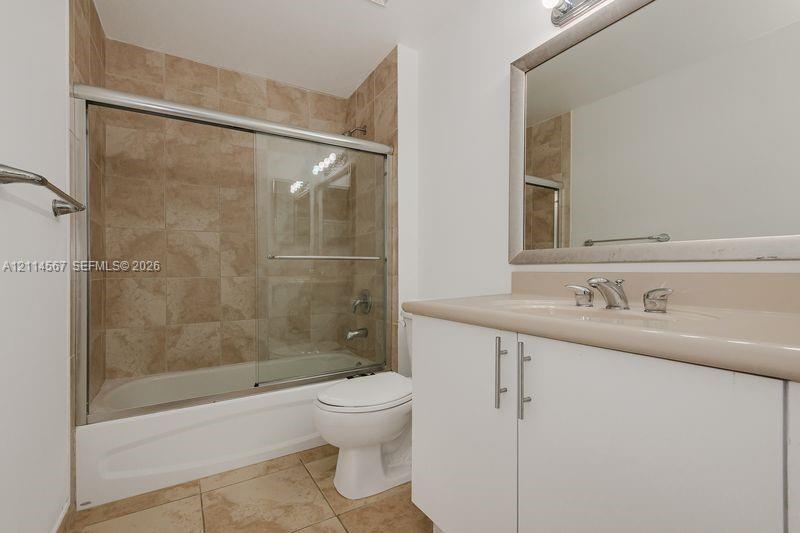 Bathroom featuring a tub-shower combination with sliding glass doors, neutral tile surround, white cabinetry, integrated sink with chrome fixtures, and a framed wall mirror