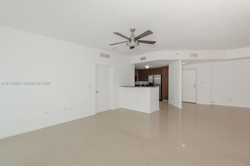 Open-concept interior featuring large-format tile flooring, a central ceiling fan, a breakfast bar with stone-surface countertop, and wood-finish cabinetry