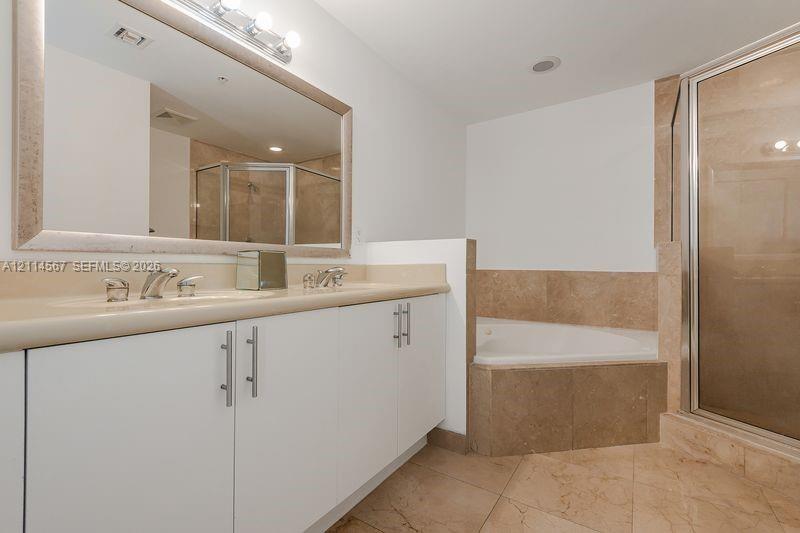 Bathroom featuring a dual-sink vanity with a stone countertop, a large framed wall mirror, a built-in soaking tub, and a separate glass-enclosed shower stall with tile surround