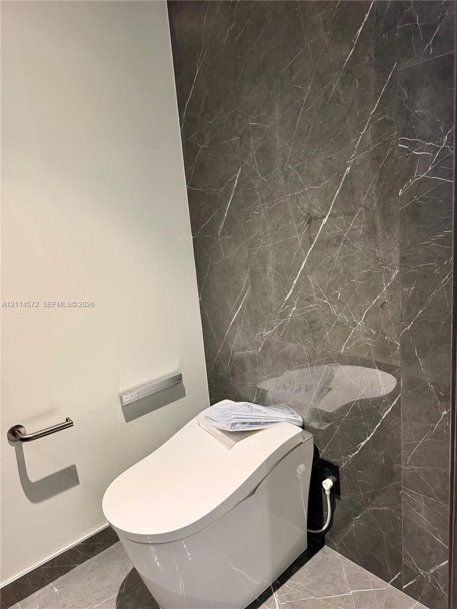 Modern restroom featuring full-height charcoal-toned stone wall cladding, matching stone floor tile, and a contemporary low-profile toilet with integrated flush system and brushed nickel hardware