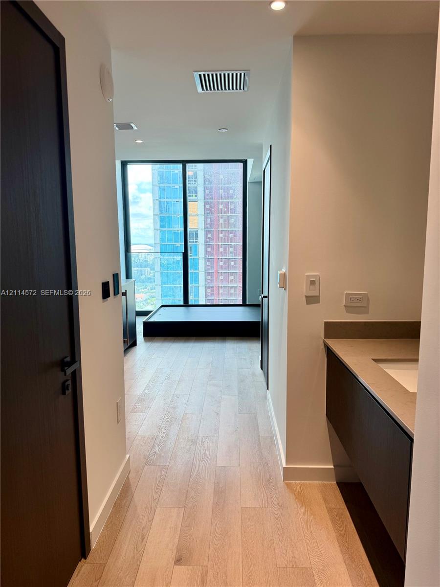 Floor-to-ceiling windows, wood-finish flooring, floating vanity with a neutral-toned countertop, and dark-toned interior doors